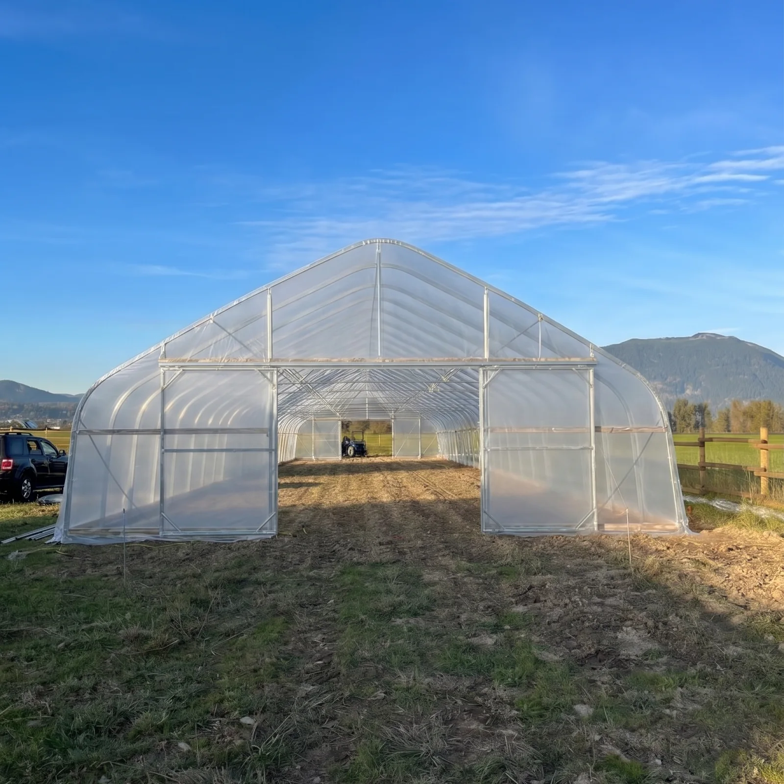 Sun & Steel high tunnel in Abbotsford, BC with both ends open, tilled beds inside and a tractor working the ground