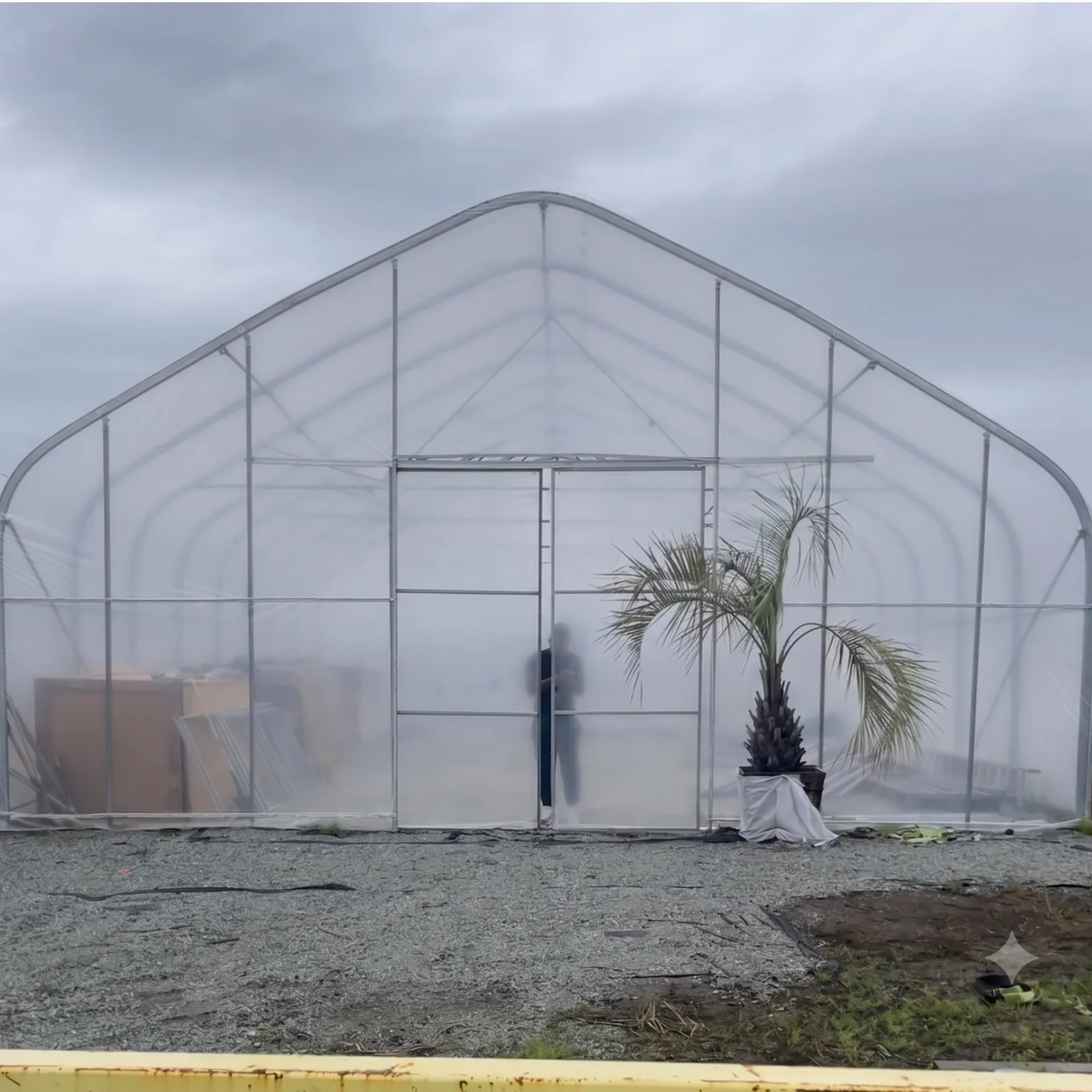 Sun & Steel high tunnel in Richmond, BC used for covered storage, with palms and stock kept inside on a gravel pad